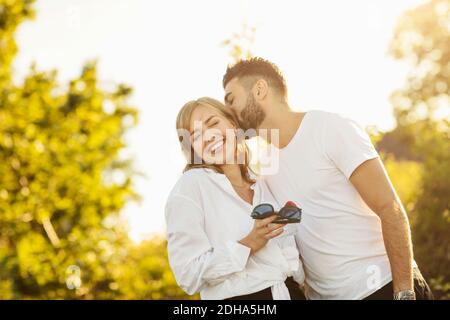 Liebevoller Mann küsst Freundin beim Stehen gegen klaren Himmel Stockfoto