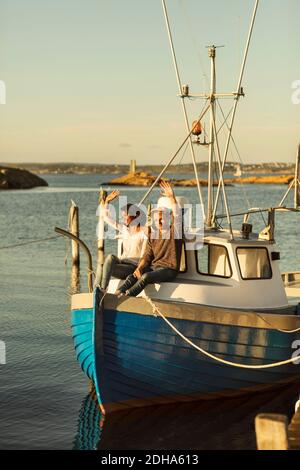 Paar mit erhobenen Händen sitzen auf einem festgetäuten Boot gegen klar Himmel im Sommer Stockfoto