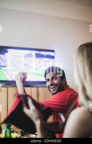 Lächelnder junger Mann, der eine Freundin anschaut, während er Fußball schaut Spiel zu Hause Stockfoto