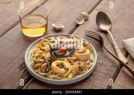 Pasta mit Meeresfrüchten. Tagliolini mit Muscheln, Garnelen, Muscheln und Tintenfischringen, mit einem Glas Wein auf einem rustikalen Holzhintergrund Stockfoto
