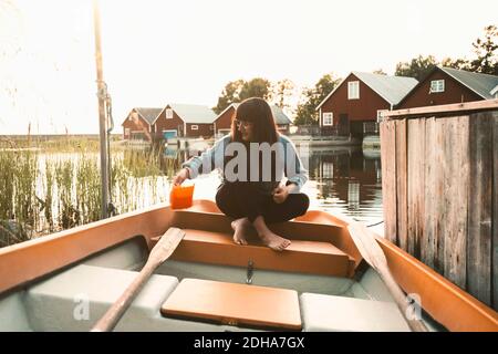 Volle Länge der Frau sitzt im Boot auf See gegen Chalets Stockfoto