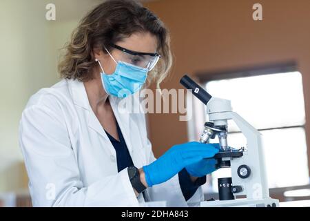 Lehrerin trägt Gesichtsmaske und Schutzbrille mit Mikroskop Im Labor Stockfoto