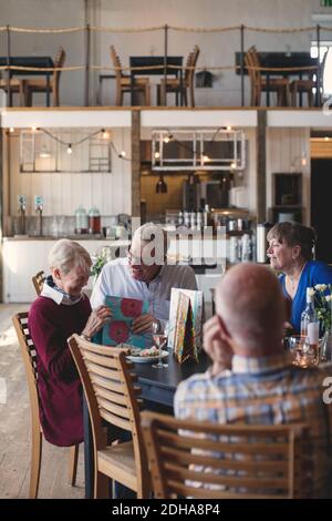 Glückliches Seniorenpaar, das präsent hält, während es mit Freunden zu Mittag geht Im Restaurant Stockfoto