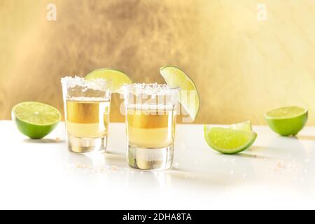 Goldene Tequila-Aufnahmen mit Salz, Limettenscheiben und Kopierraum Stockfoto