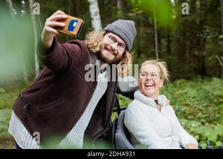 Junge männliche Hausmeister, die Selfie mit behinderten Frau im Wald Stockfoto