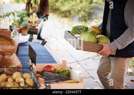 Mittelteil des Mannes mit Gemüsebehälter, der am Marktstand steht Stockfoto