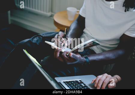 Mittelteil des Geschäftsmannes, der im Tagebuch schreibt, während Kollege Laptop benutzt Im kreativen Büro Stockfoto