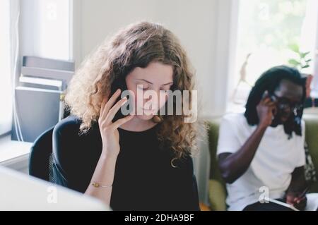 Junge Geschäftsfrau im Gespräch auf Handy mit Kollegen im Hintergrund Im Kreativbüro Stockfoto