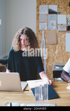 Junge Geschäftsfrau hält Notizblock während mit Laptop am Tisch in Kreatives Büro Stockfoto