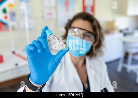 Weibliche Lehrerin trägt Gesichtsmaske und Schutzbrille mit einem Reagenzglas mit Impfstoff-Text Stockfoto