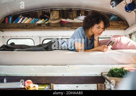 Junge Afro-Frau, die im Liegen über das Handy surft Bett im Wohnheim Stockfoto