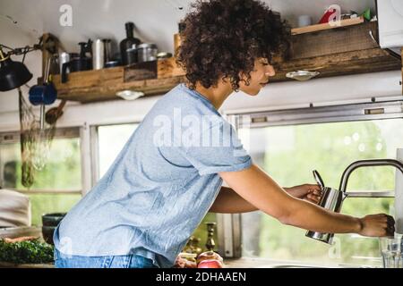 Seitenansicht einer Afro-Frau, die den Wasserkocher aus dem Wasserhahn füllte Wohnmotorhaus Stockfoto