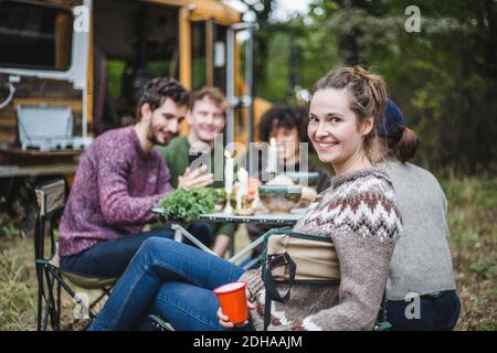 Portrait von lächelnden blonden Frau sitzen Freunde am Tisch Wohnwagen im Wald während des Campens Stockfoto