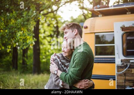 Lächelndes mittelerwachsenes Paar umarmt beim Camping im Wald Stockfoto