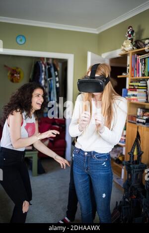 Fröhliche Teenager-Mädchen Blick auf Freund trägt Virtual Reality-Headset Zu Hause Stockfoto