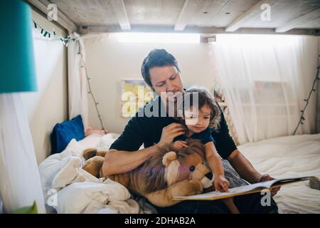 Vater liest Buch mit Tochter, während sie im Schlafzimmer sitzt Stockfoto