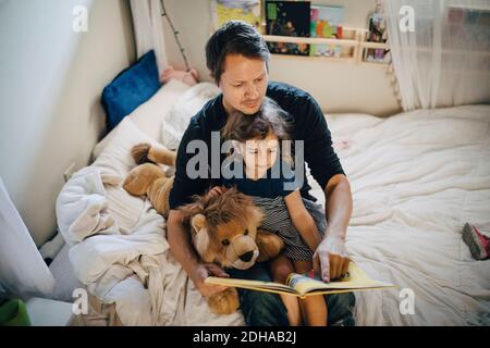 High-Angle-Ansicht des Vaters Buch mit Tochter lesen, während Im Schlafzimmer sitzen Stockfoto