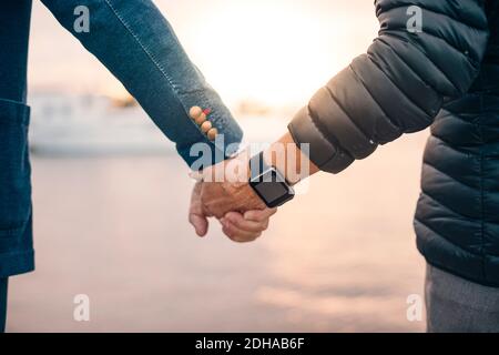 Zugeschnittenes Bild einer älteren Frau, die eine Smart Watch trägt, während sie hält Hand des Mannes am Hafen Stockfoto