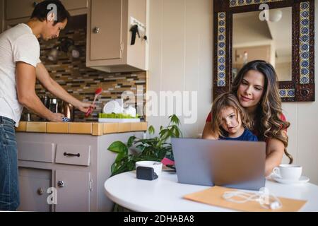 Mutter und Tochter mit Laptop, während Vater in der Küche arbeitet Stockfoto