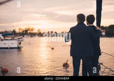 Rückansicht des älteren Ehepaares, das auf dem Bug der Yacht steht Bei Sonnenuntergang Stockfoto