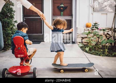 Tochter Skateboarding mit Hilfe der Mutter, während Sohn sitzt auf Dreirad Stockfoto