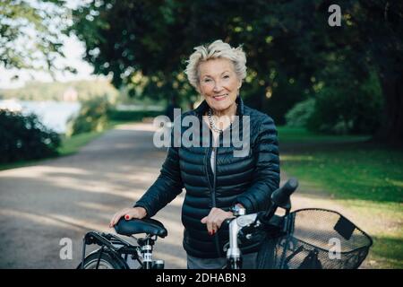 Porträt einer lächelnden älteren Frau mit Fahrrad im Park Stockfoto