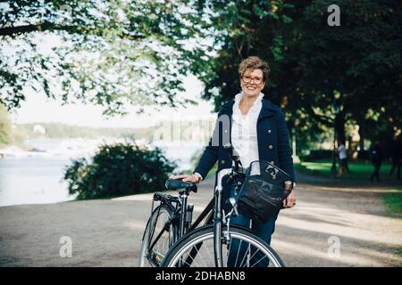 Porträt einer lächelnden älteren Frau mit Fahrrad im Park stehen Stockfoto