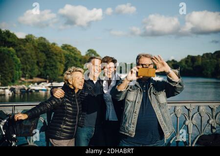 Lächelnde männliche und weibliche Freunde, die Selfie mit dem Smartphone machen Geländer der Brücke Stockfoto