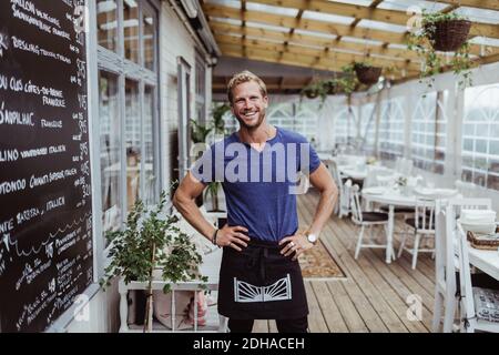 Porträt eines lächelnden männlichen Besitzers mit der Hand auf der Hüfte stehend Im Restaurant Stockfoto