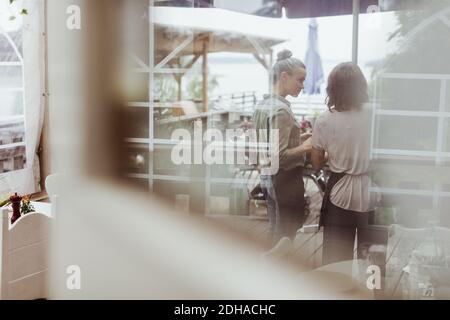 Rückansicht von Geschäftsfrauen, die im Restaurant durch Glas gesehen stehen Angezeigt Stockfoto