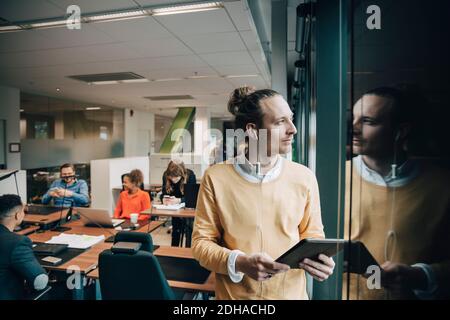 Nachdenklicher Geschäftsmann hält digitale Tablette Blick durch Fenster im Büro Stockfoto