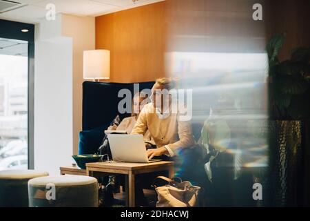 Ein Geschäftsmann schaut weg, während er mit einem Laptop von einem Kollegen sitzt Büro Cafeteria aus Glas gesehen Stockfoto