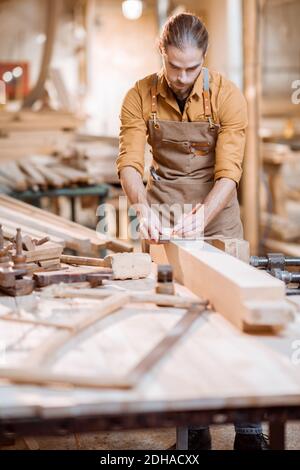 Schöner Zimmermann, der mit dem Holz arbeitet, die Planke mit dem Bleistift in der Schreinerei kennzeichnend Stockfoto