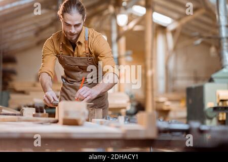 Schöner Zimmermann, der mit dem Holz arbeitet, die Planke mit dem Bleistift in der Schreinerei kennzeichnend Stockfoto