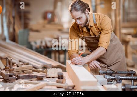 Schöner Zimmermann, der mit dem Holz arbeitet, die Planke mit dem Bleistift in der Schreinerei kennzeichnend Stockfoto