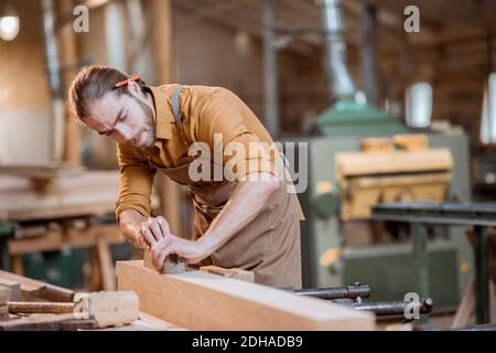 Schöner Zimmermann, der mit dem Holz arbeitet, die Bar mit dem Flugzeug in der Schreinerei hobeln Stockfoto