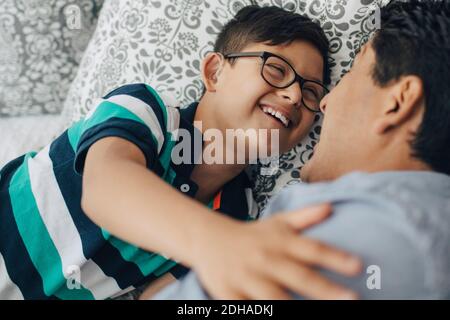 Glücklicher behinderter Junge, der den Vater ansah, während er auf dem Bett lag Zu Hause Stockfoto