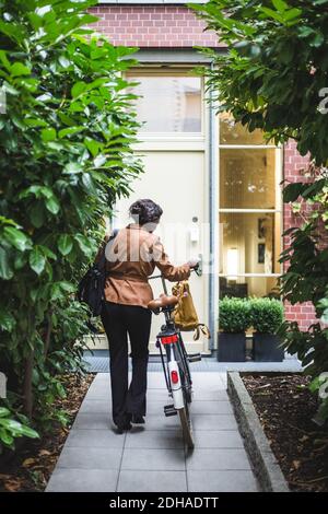 Rückansicht einer Architektin mit Fahrrad, das gegen das Haus steht Stockfoto