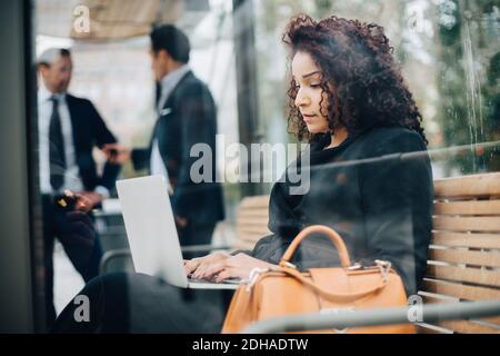 Seitenansicht einer Geschäftsfrau mittleren Erwachsenen mit Laptop Busschutzhaus aus Glas gesehen Stockfoto