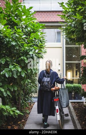 Rückansicht einer Architektin mit Fahrrad, das gegen das Haus läuft Stockfoto