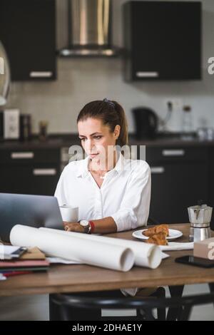 Freiberuflerin mit Laptop, während sie mit Kaffeetasse sitzt Zu Hause Stockfoto