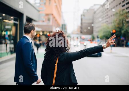Geschäftsmann steht neben Geschäftsfrau, die Taxi auf der Straße in der Stadt hagelt Stockfoto