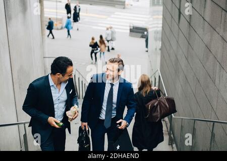 Blickfeld auf lächelnde, reife männliche Geschäftskollegen, die sich bewegen Oben auf der Treppe in der Stadt Stockfoto