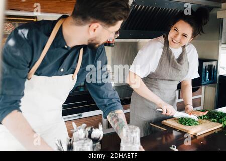 Lächelnde Unternehmerin schneiden Gemüse während der Arbeit mit männlichen Partner In Nutzfahrzeug Stockfoto