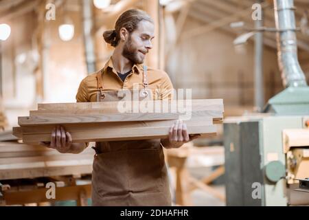 Zimmermann trägt Kiefernplanken in einer Schreinerei Werkstatt Lager. Rohstoffe für die zukünftige Holzbearbeitung vorbereiten Stockfoto