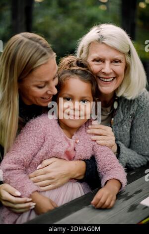 Porträt einer lächelnden Familie aus mehreren Generationen, die am Tisch im Hinterhof sitzt Stockfoto