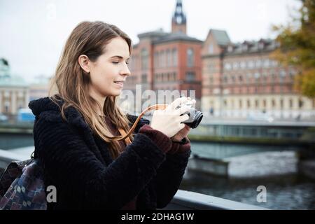 Lächelnde junge Frau mit Kamera auf Brücke in der Stadt stehen Stockfoto