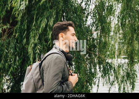 Seitenansicht des jungen Mannes mit Rucksack, der am Baum steht In der Stadt Stockfoto