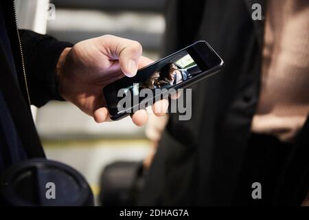 Zugeschnittenes Bild von Mann mit Smartphone, während stehen mit Freund auf der Rolltreppe Stockfoto