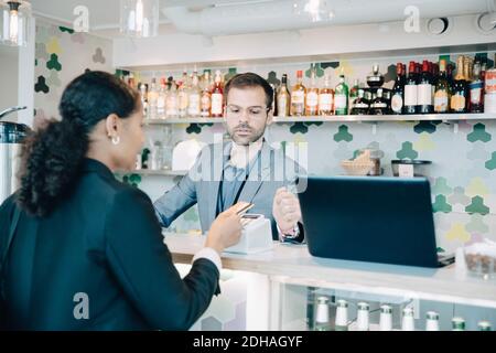 Besitzer, der eine Geschäftsfrau ansieht, die kontaktloses Bezahlen im Bürocafé macht Stockfoto